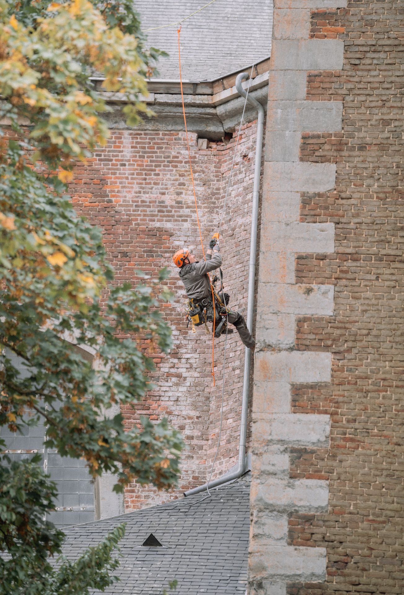 Technicien cordiste effectuant des travaux de rénovation ou d'inspection sur une façade en briques d'un bâtiment ancien.